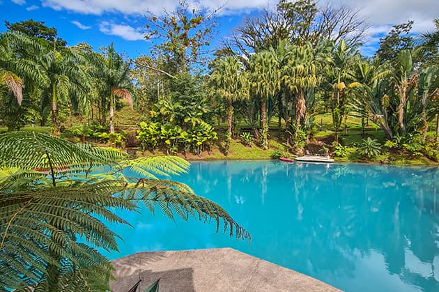 A pristine blue pond encircled by lush green palm trees and vibrant vegetation rests beneath a partly cloudy sky during the Cathedral Waterfall Expedition at Rincón de la Vieja.