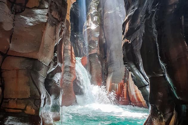 Experience the Cathedral Waterfall Expedition in Rincón de la Vieja, where a rocky gorge unveils a stunning waterfall cascading into turquoise waters, all beautifully illuminated by the warm sunlight.