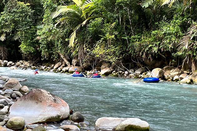 Tubing enthusiasts enjoy a ride down the river amidst lush greenery and rocks, capturing the scenic beauty typical of Tubing in Rincón de la Vieja.