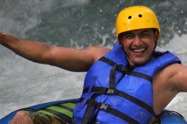 A person beams with joy while participating in Tubing in Rincón de la Vieja, sporting a yellow helmet and blue life vest amidst the vibrant waters.