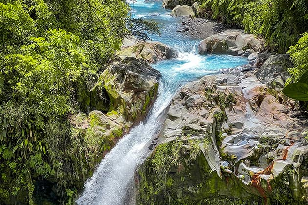 Nestled in the heart of Rincon de la Vieja, a waterfall cascades into a rocky stream, embraced by lush green foliage.