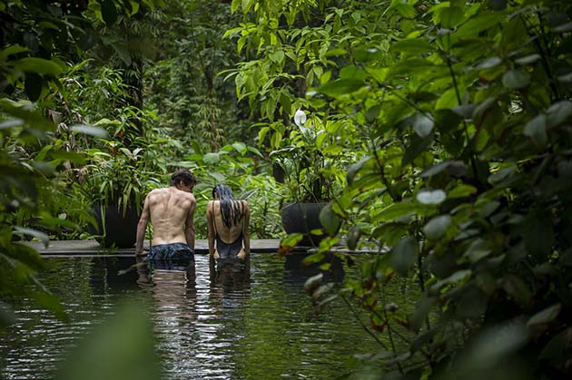 Two people stand in a shallow pool, enveloped by the lush green foliage of Rincon de la Vieja.